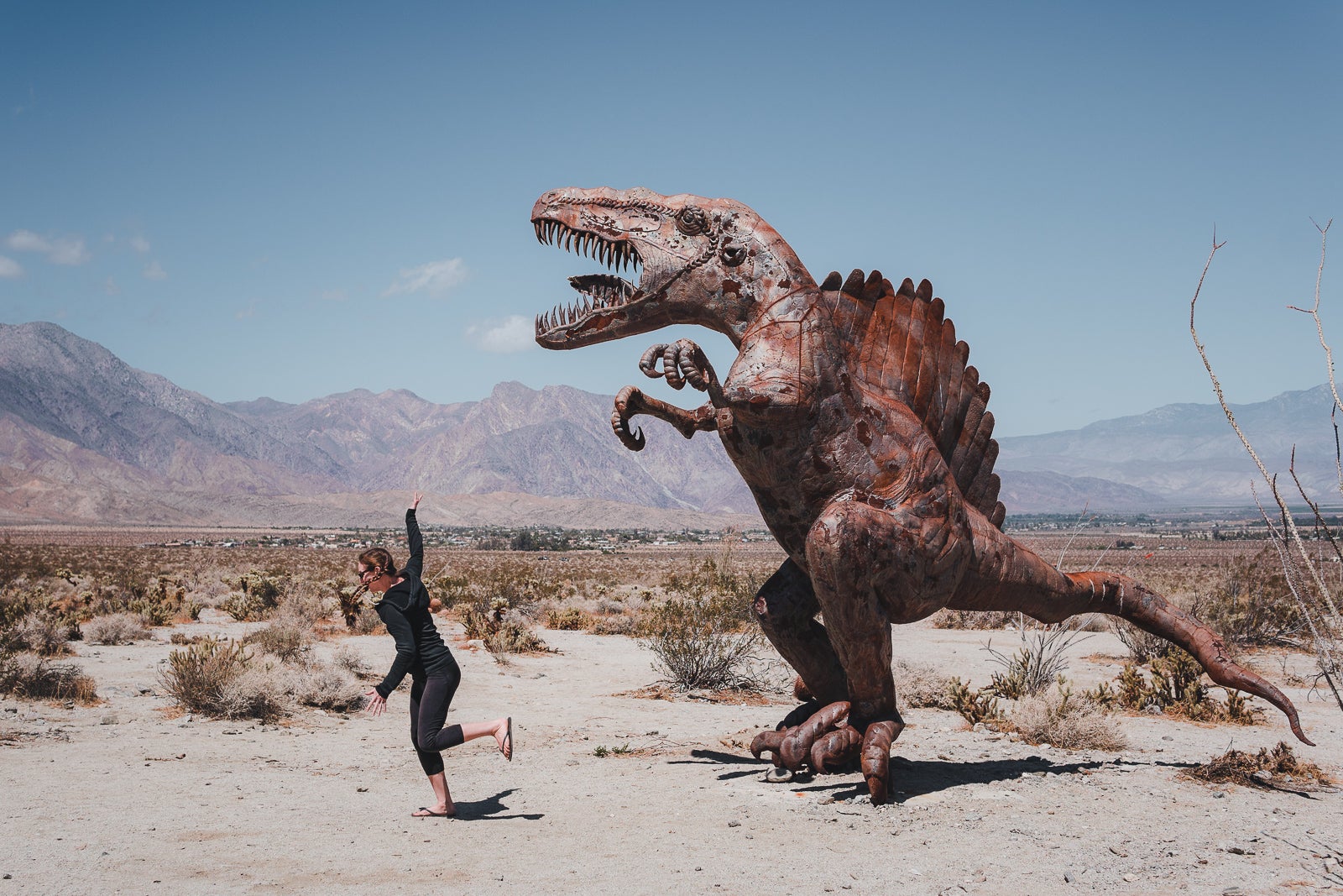 woman poses for photo running away from a dinosaur sculpture in the anza-borrego desert