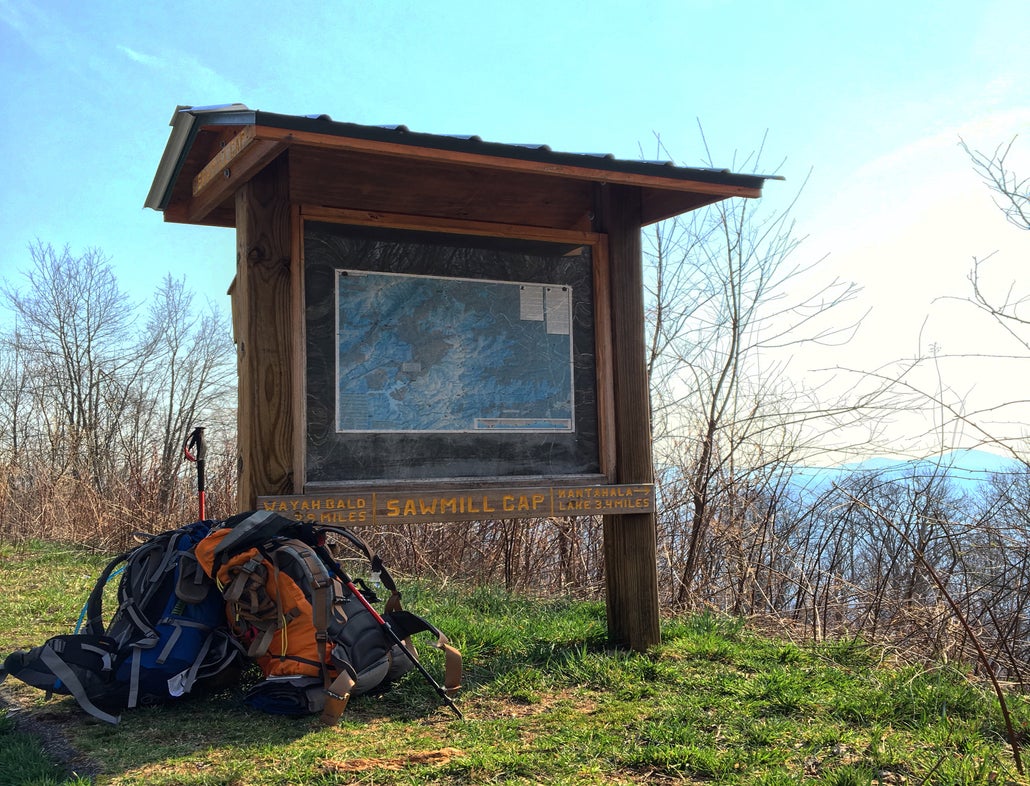 a pair of loaded backpacks rest under an informational sign on a hiking trail