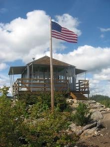 American flag flying in a stiff breeze in front of a lookout building under cloudy blue sky.



Gold butte lookout

Credit: USFS