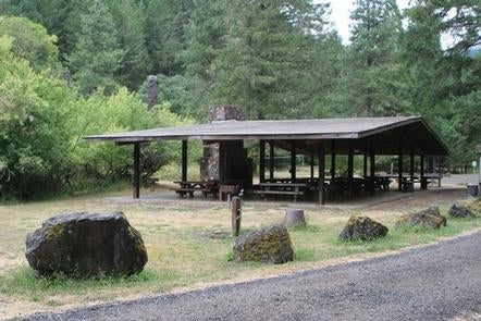 Large picnic shelter with stone fireplace and chimney and boulders lining a gravel road in front of fir forest and shrubs.



Wolf creek group site

Credit: USFS
