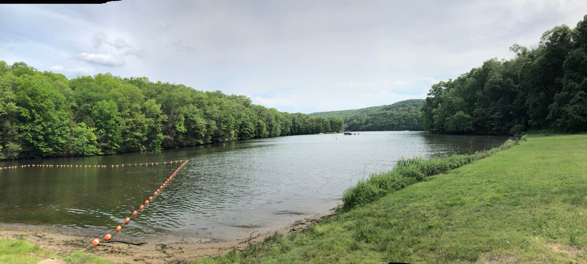 River with portion roped off as a swimming area surrounded by green forests and lawn.