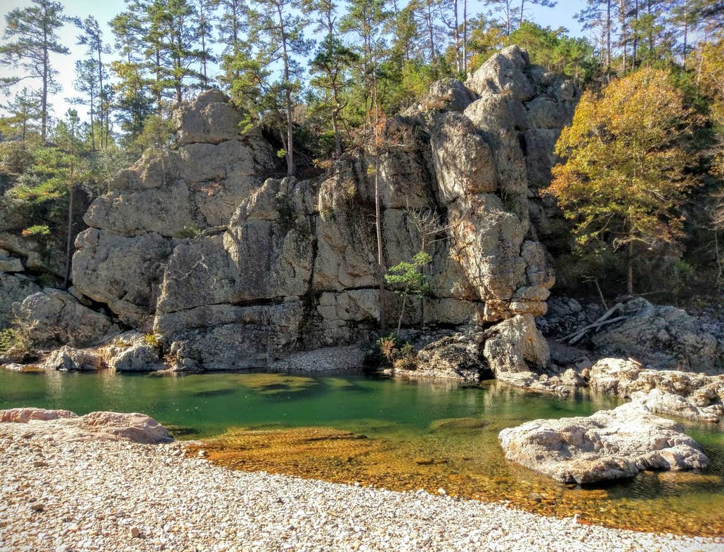 A rock wall looks down upon a clear water river in the Ouachita National Forest