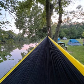 Picture of hammock with river view and campsites with water view in the background.