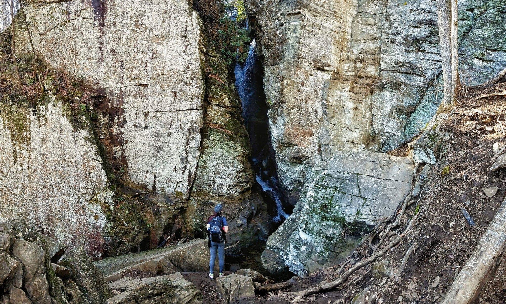 hiker in the distance looks up at the large raven cliff falls in front of him