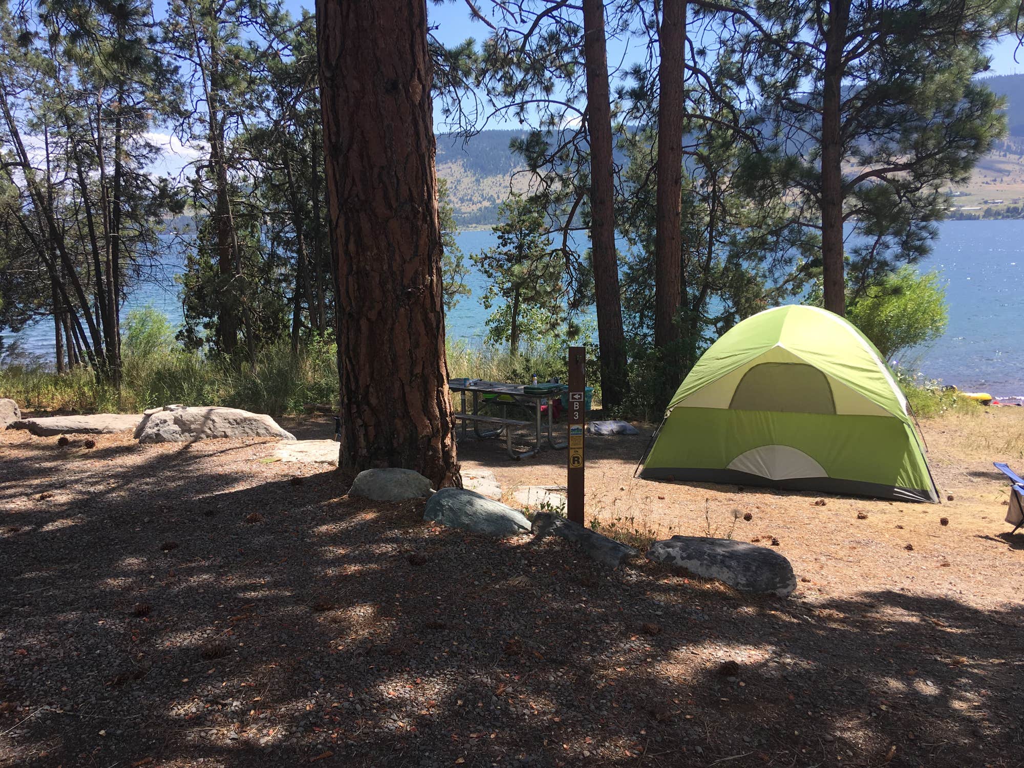 Freen tent at lakeside forested campsite.