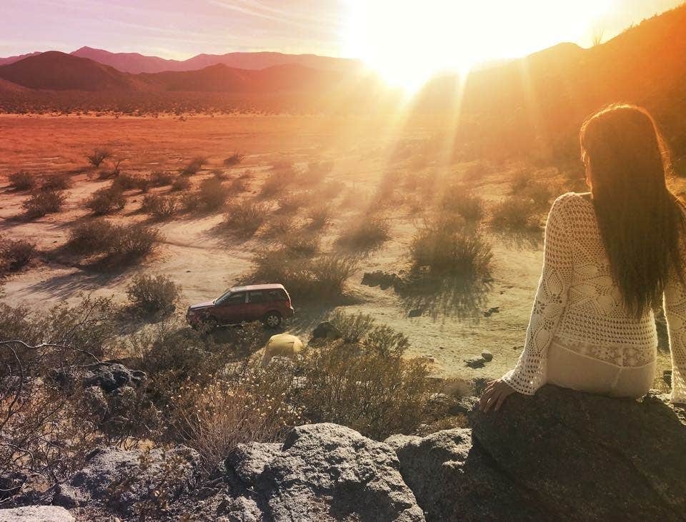 female camper facing sun rays as they cascade over Blair Valley Campground